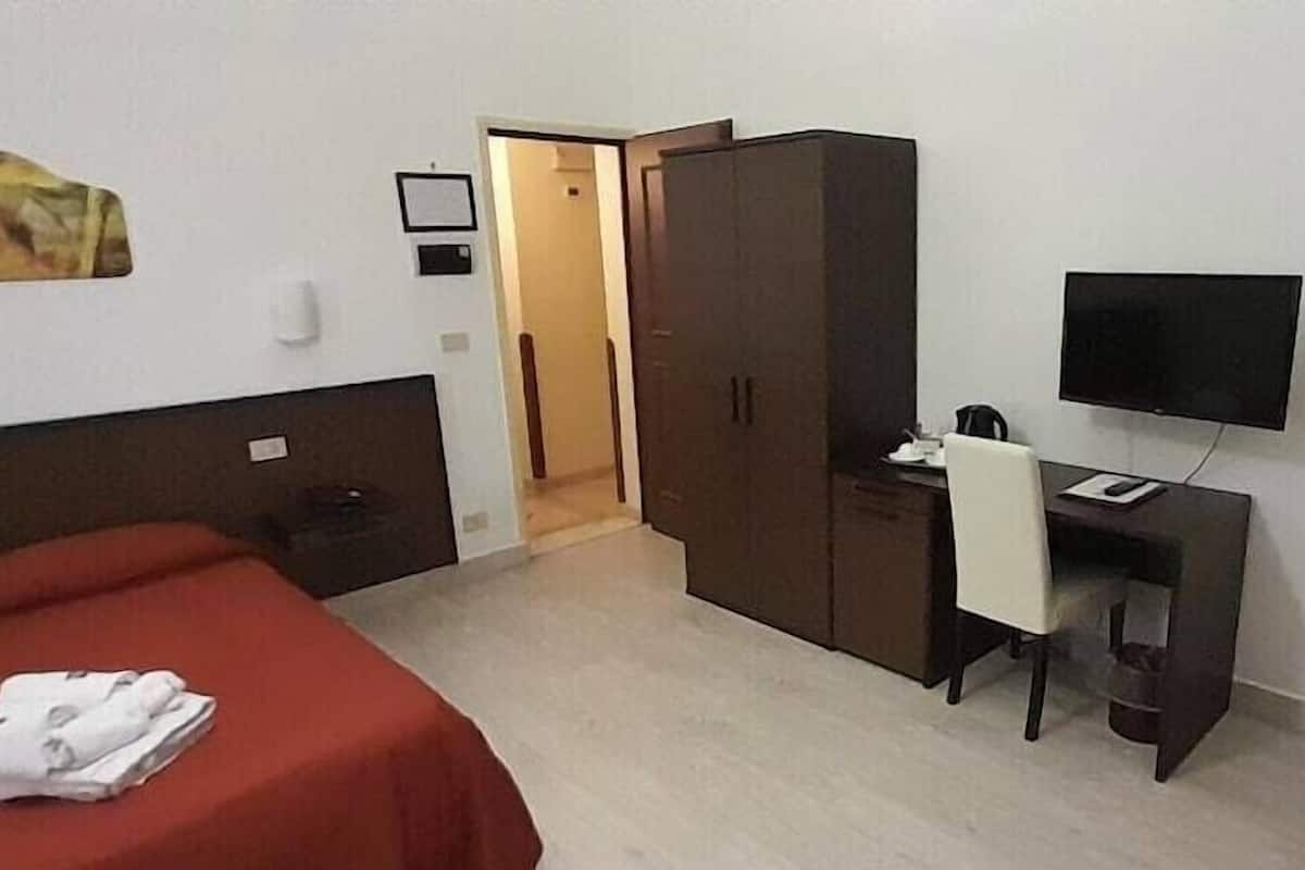 Habitación de hotel con cama, escritorio, armario, televisor y puerta que da a otra habitación.