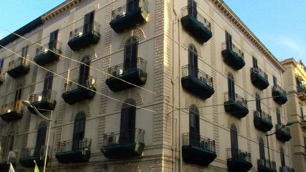 A multi-story building with balconies, a street sign, parked cars, and a flag. - Hotel Tonic (Palermo)