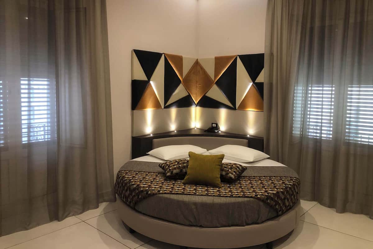 Un dormitorio moderno con cama redonda, diseño geométrico en la pared y cortinas traslúcidas.