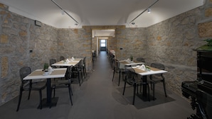A long dining area with stone walls, tables set with white tablecloths, and black chairs. - Hotel Tonic (Palermo)