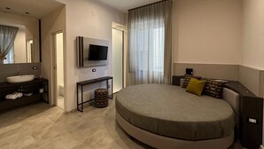 A modern bedroom with a large bed, a TV mounted on the wall, a bedside table, and a bathroom with a sink and mirror. - Hotel Tonic (Palermo)