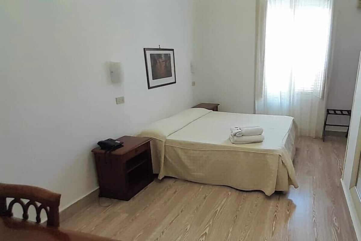 Una habitación pequeña y sencilla con una cama, una mesita de noche, una silla y un cuadro en la pared.