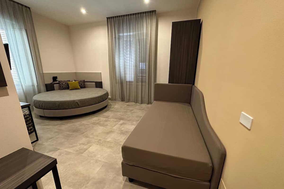 Un dormitorio compacto con cama, sofá, una mesita y una ventana con cortinas.