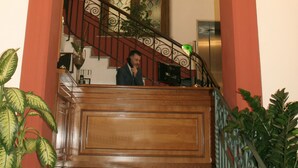 A grand staircase with a red archway, a wooden handrail, and a glass door with decorative patterns. - Hotel Tonic (Palermo)