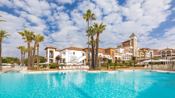 A resort with a large pool, palm trees, and Mediterranean-style buildings.