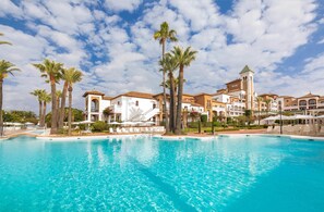 A resort with a large pool, palm trees, and Mediterranean-style buildings. - Barceló Isla Canela (Ayamonte)