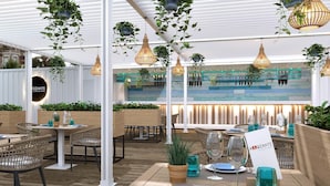 An outdoor dining area with wicker chairs, tables set for dining, hanging plants, and pendant lights.