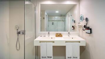 Un baño moderno con ducha de vidrio, un espejo grande y dos lavamanos con toallas colgando debajo.