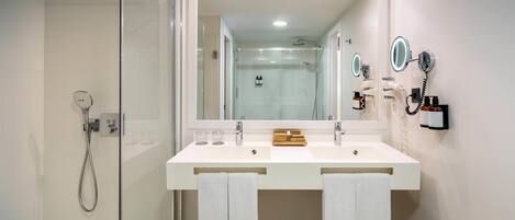 Un baño moderno con ducha de vidrio, un espejo grande y dos lavamanos con toallas colgando debajo.