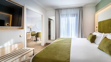 Ein Hotelzimmer mit einem großen Bett, einem an der Wand montierten Fernseher, einem Schreibtisch mit Stuhl und Blick durch ein Fenster nach draußen.