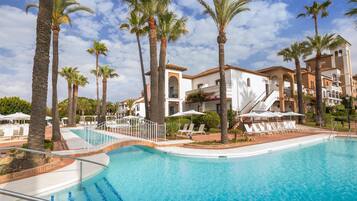 A swimming pool with palm trees, lounge chairs, and a building with a tiled roof.