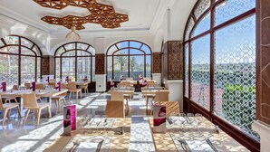 A spacious dining area with high arched windows, wooden furniture, and a decorative ceiling.