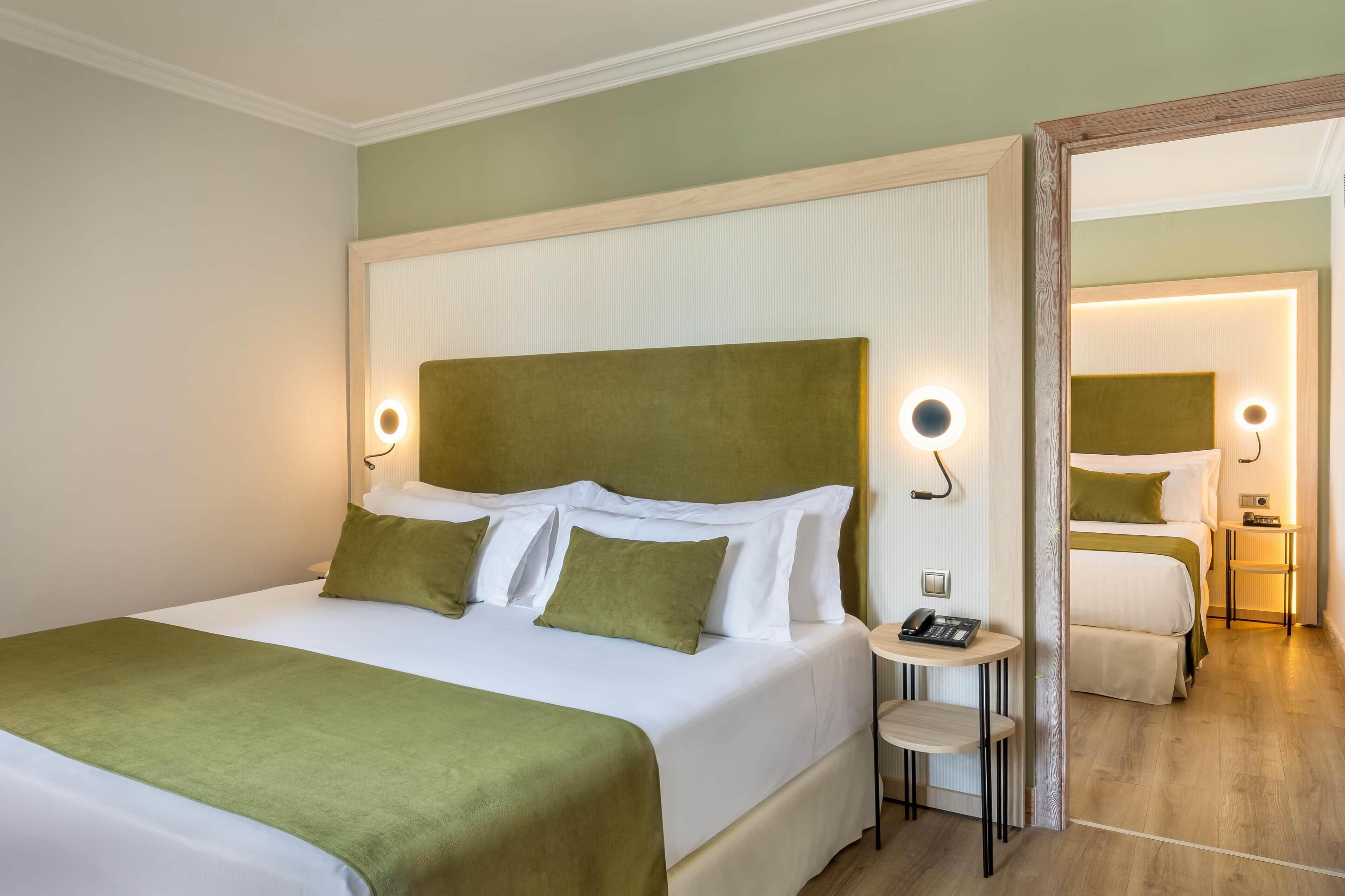A hotel room with a large bed, bedside tables, a mirror, and a small table with a phone.