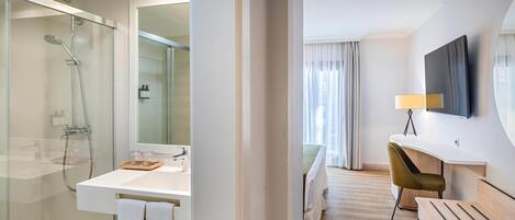 A modern hotel bathroom with a glass-enclosed shower, a white sink, and a large mirror.