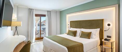 Habitación de hotel con cama, escritorio, silla, mesita de noche y vistas al exterior.