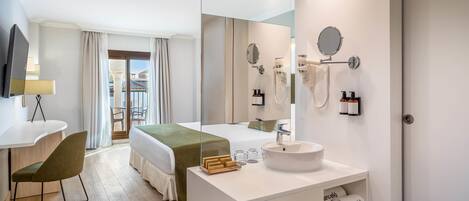 Habitación de hotel con cama, escritorio con silla, un espejo grande, lavamanos y armario.