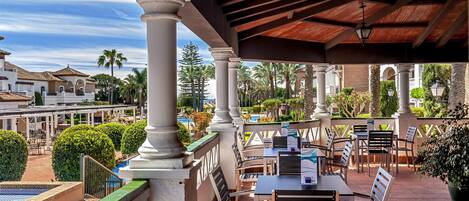 An outdoor patio area with tables and chairs, surrounded by greenery and palm trees.
