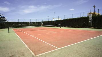 A tennis court with a net, surrounded by a fence and trees.