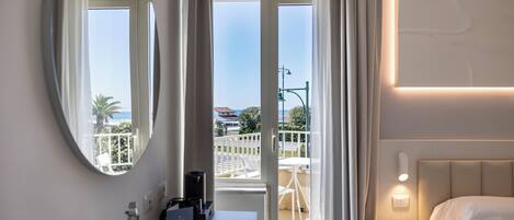 A hotel room with a bed, a bedside table, a mirror, a window with curtains, and a view of the outside.