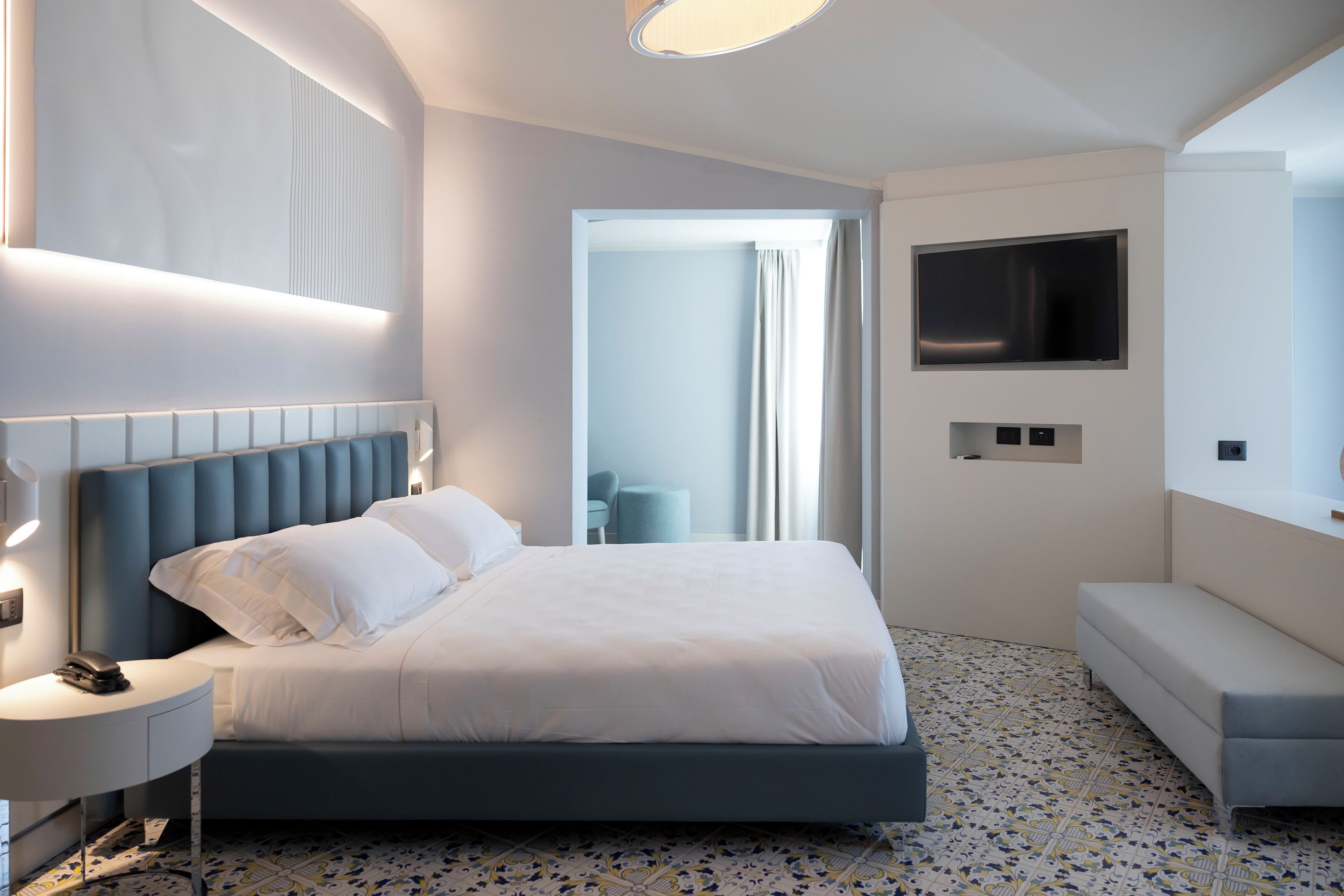 A modern hotel room with a large bed, bedside table, and a TV mounted on the wall.