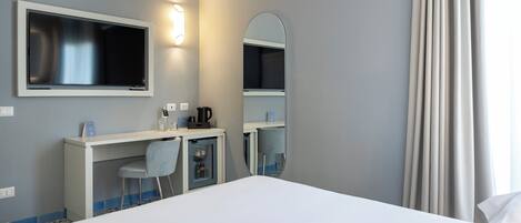 Quarto de hotel com cama, escrivaninha, cadeira, espelho e televisão.