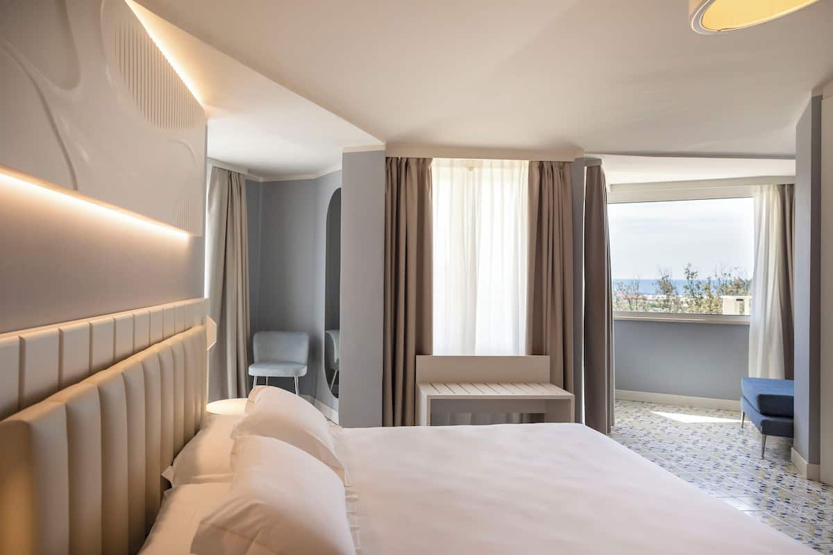 A hotel room with a large bed, a small table, a chair, and a view of the outdoors.