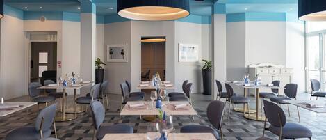 Un comedor de hotel con varias mesas, sillas e iluminación colgante.
