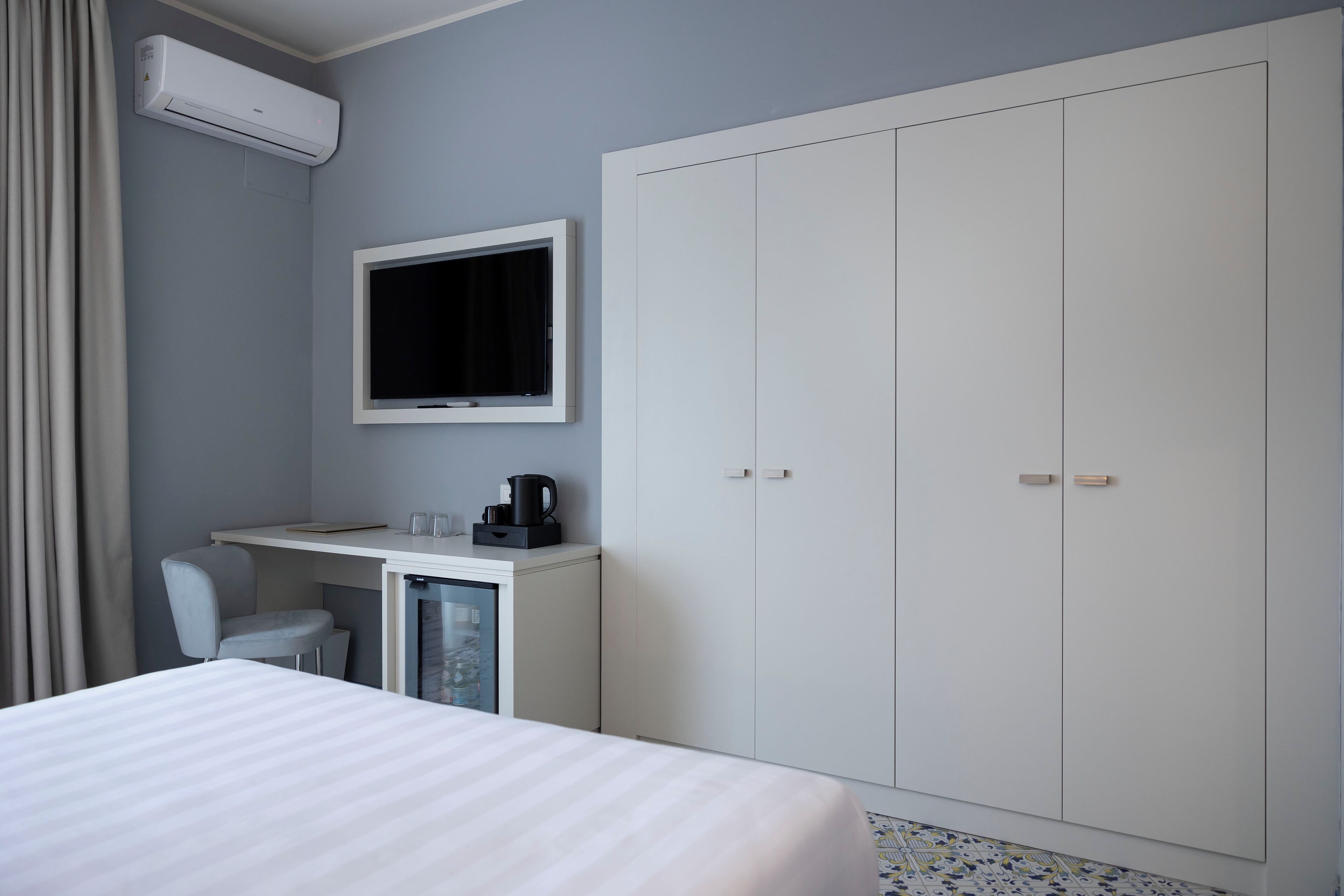 A hotel room with a bed, a desk with a chair, a television, and a wardrobe.