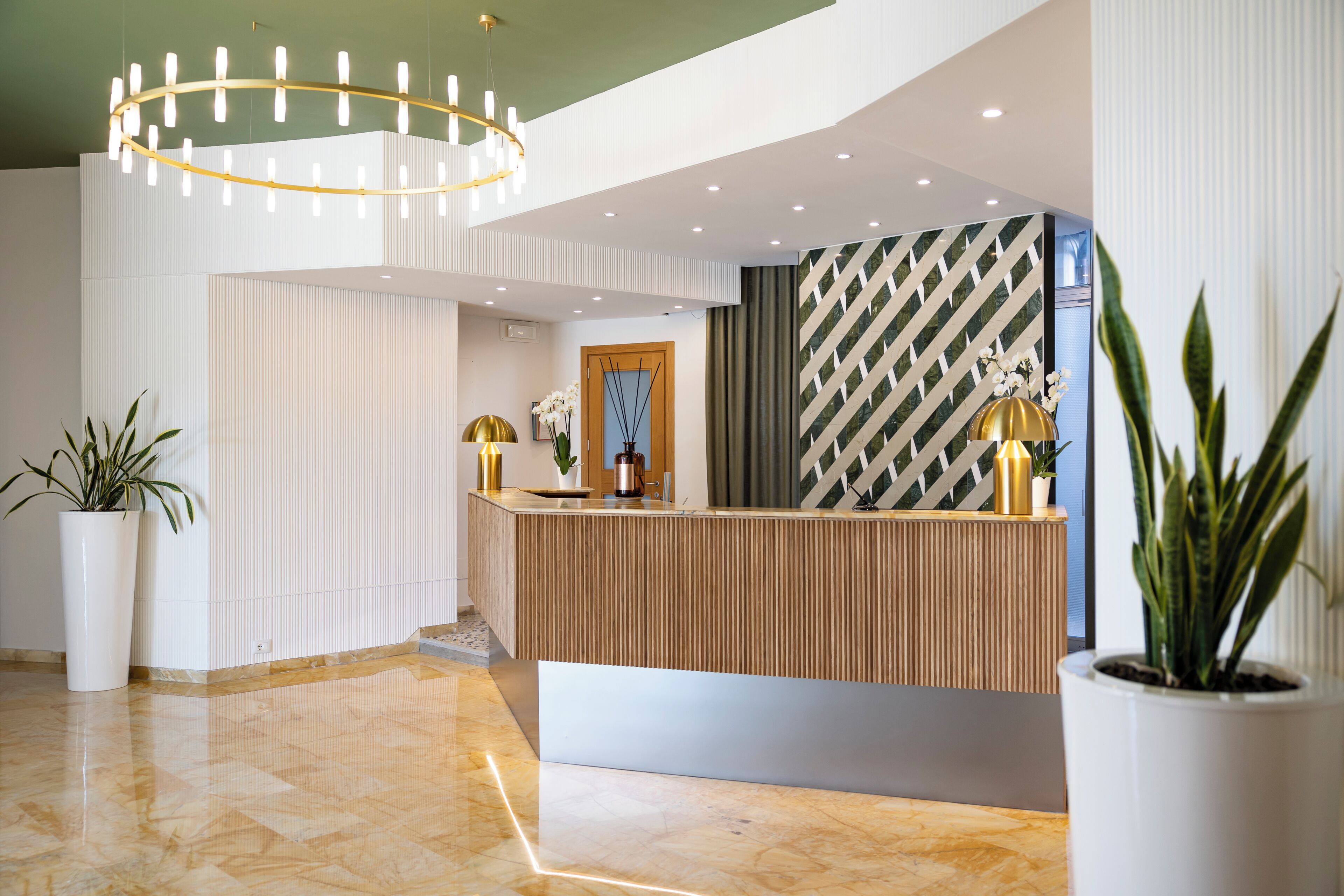 Un área de recepción con un mostrador de madera, plantas en macetas, un candelabro y un papel tapiz estampado.