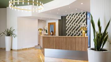 Un área de recepción con un mostrador de madera, plantas en macetas, un candelabro y un papel tapiz estampado.