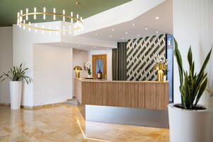 Un área de recepción con un mostrador de madera, plantas en macetas, un candelabro y un papel tapiz estampado.