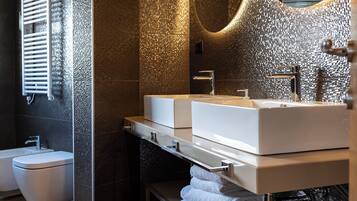 Un baño moderno con lavamanos doble, inodoro y un banco con toallas.