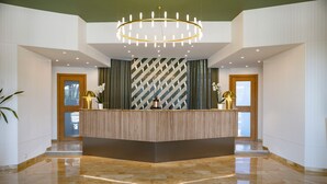 A reception desk with a patterned backdrop, a chandelier, and a polished marble floor. - Grand Hotel (Forte dei Marmi)