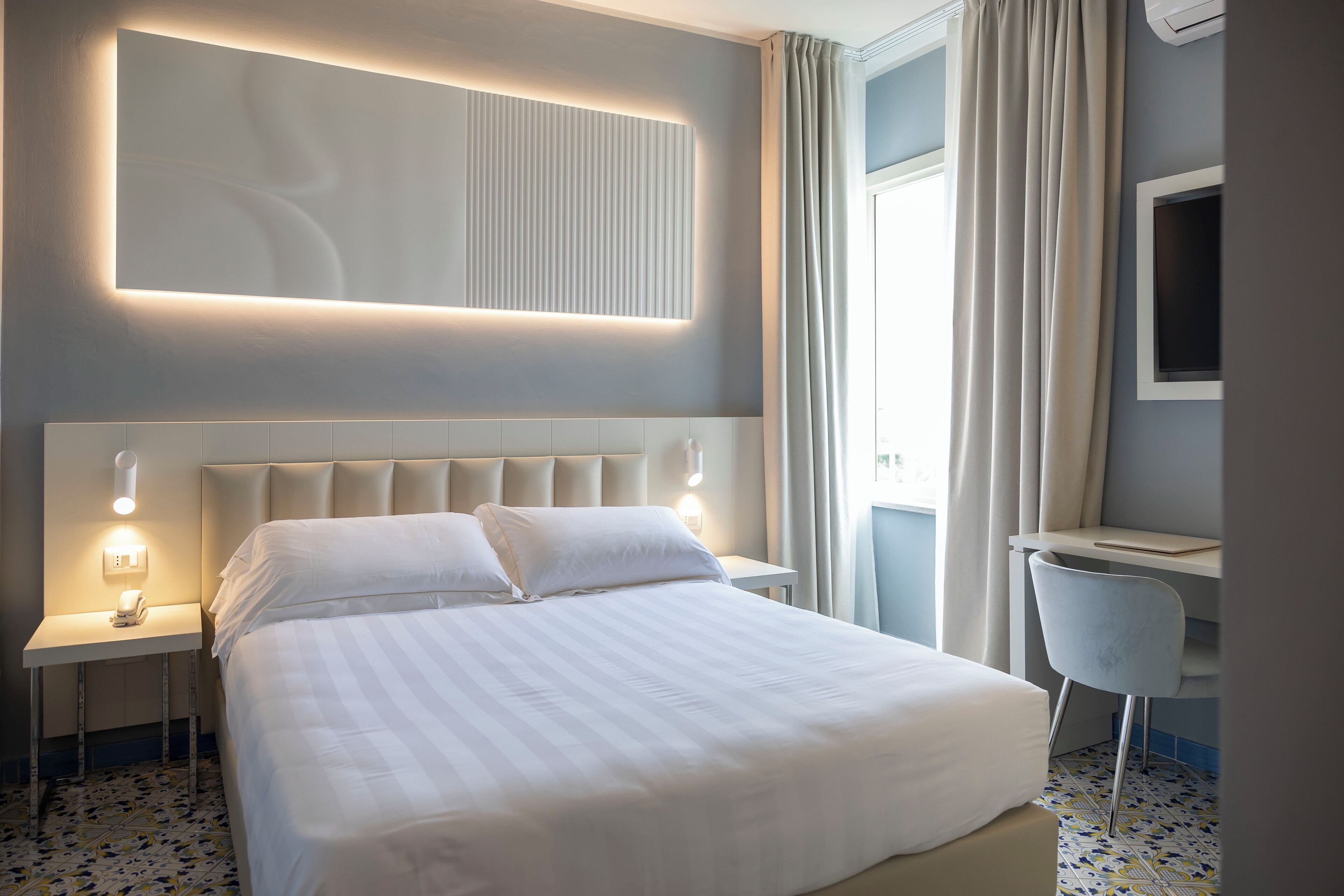 Een moderne hotelkamer met een groot bed, nachtkastjes met lampen, een bureau en een stoel.