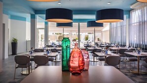A spacious hotel dining area with multiple tables, large hanging lamps, and a view of the outdoor area. - Grand Hotel (Forte dei Marmi)