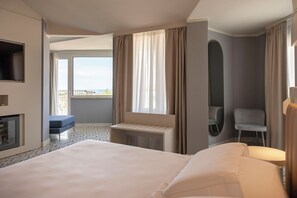 A hotel room with a large bed, a small desk, a chair, a TV, and a balcony with a view. - Grand Hotel (Forte dei Marmi)