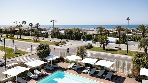 A poolside area with lounge chairs and umbrellas, a road with traffic lights, and a view of the sea. - Grand Hotel (Forte dei Marmi)
