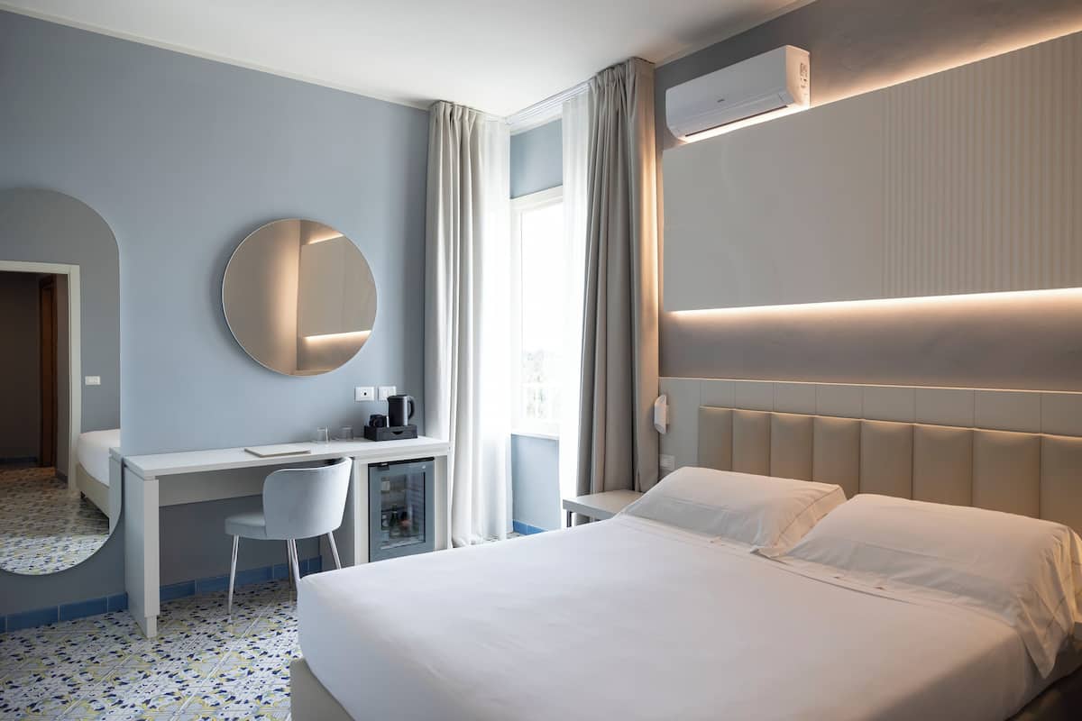 A hotel room with a bed, desk, chair, and a round mirror.