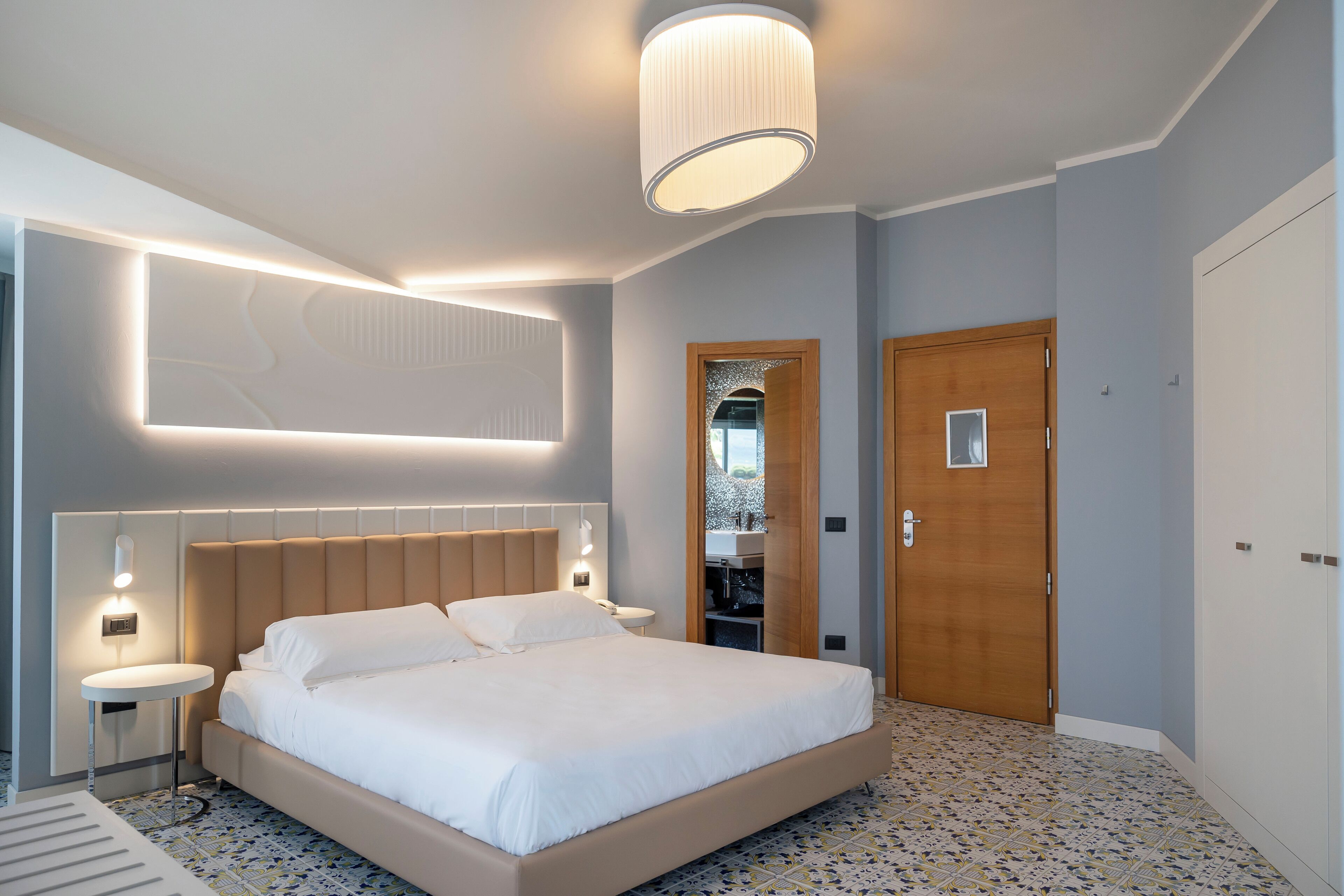 Una camera d'albergo moderna con un letto grande, comodini, uno specchio e una porta in legno.