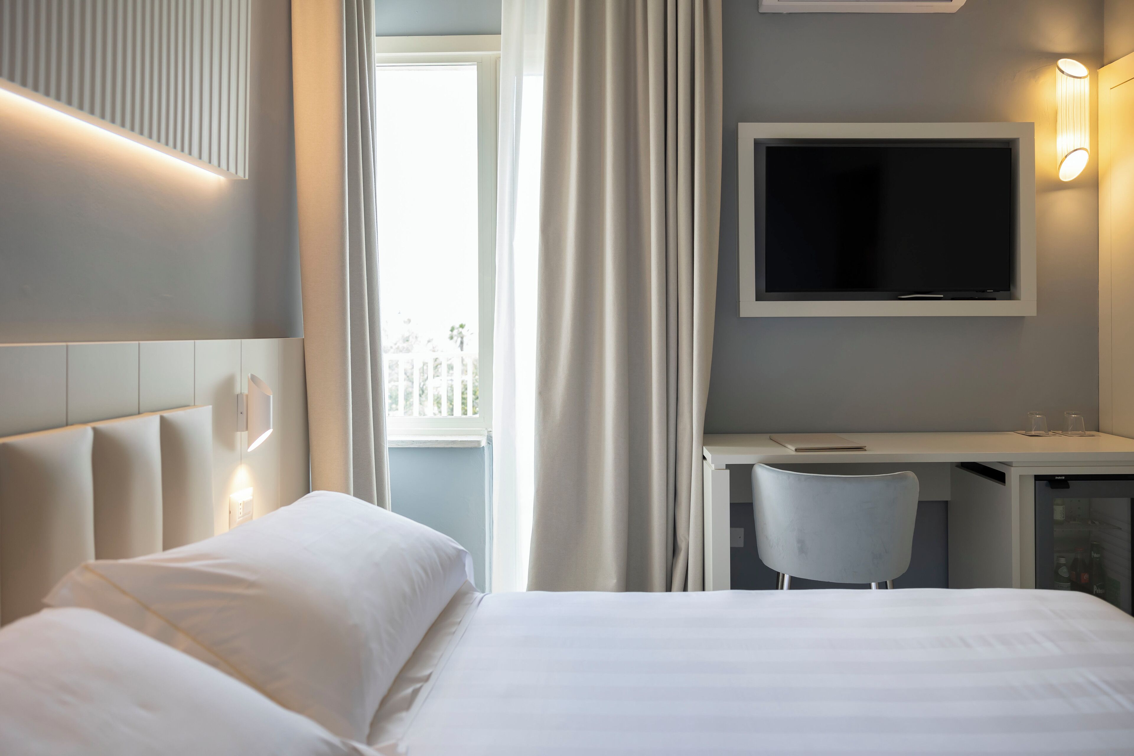 Une chambre d’hôtel avec un lit, un bureau, une chaise, une télévision et une fenêtre avec des rideaux.