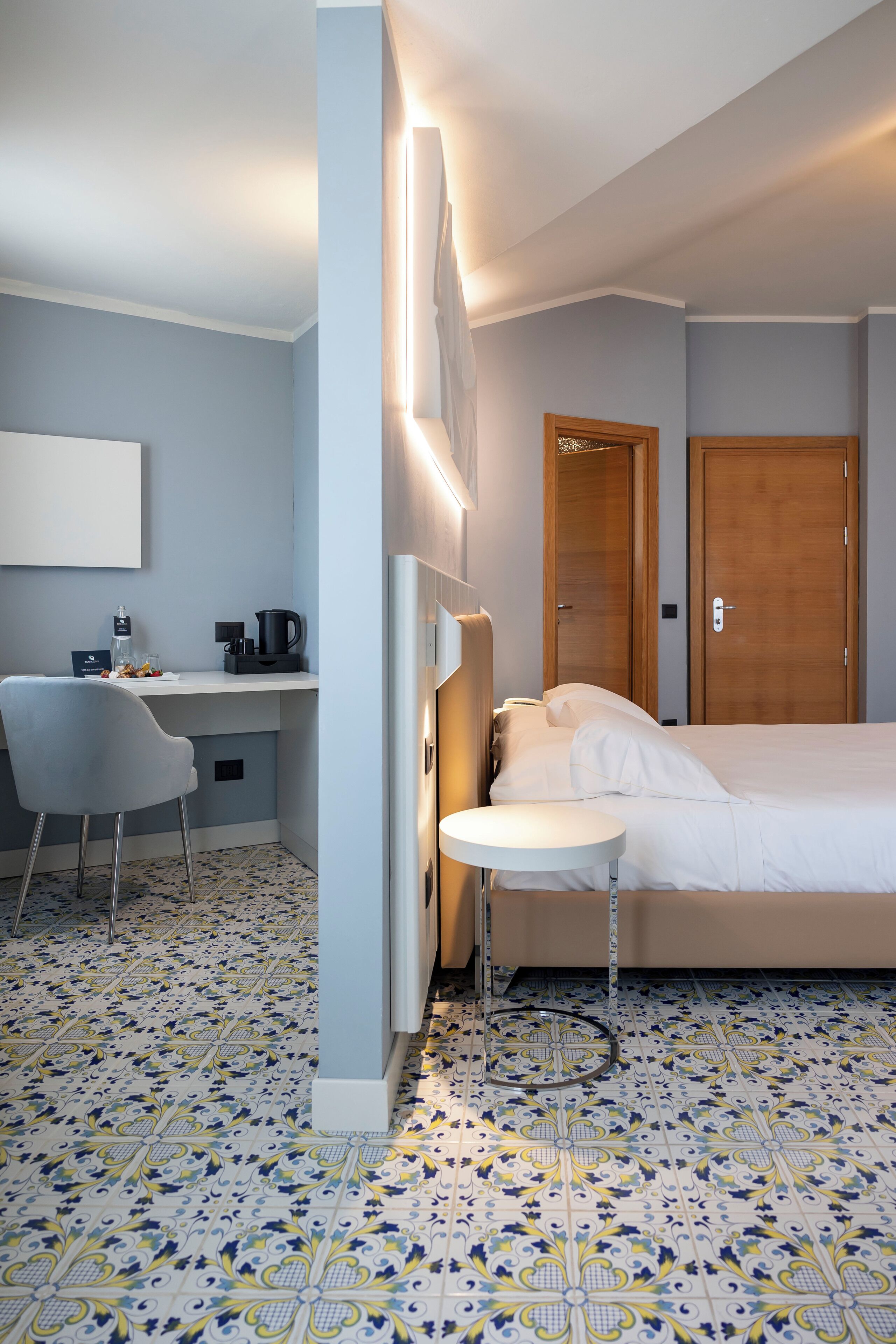 Habitación de hotel con cama, escritorio con silla, una mesita y una lámpara fijada a la pared.
