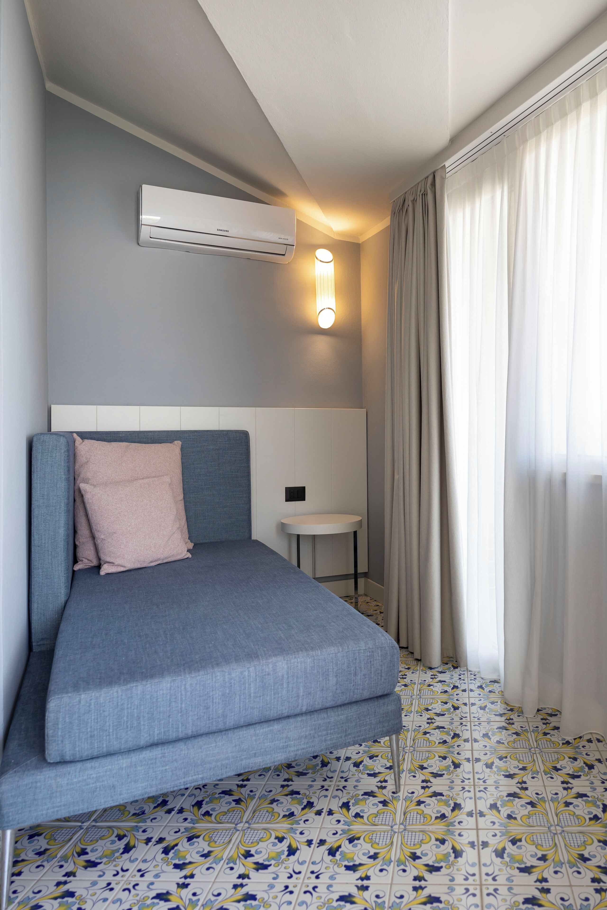 Una habitación de hotel moderna con una cama, un equipo de aire acondicionado, una mesita pequeña y un suelo decorado con baldosas.