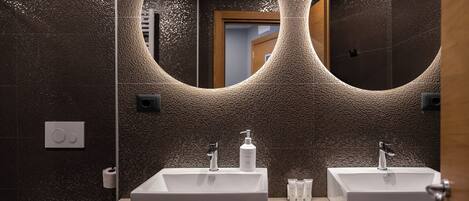 Un baño con dos lavamanos, un espejo grande y una pared con textura.