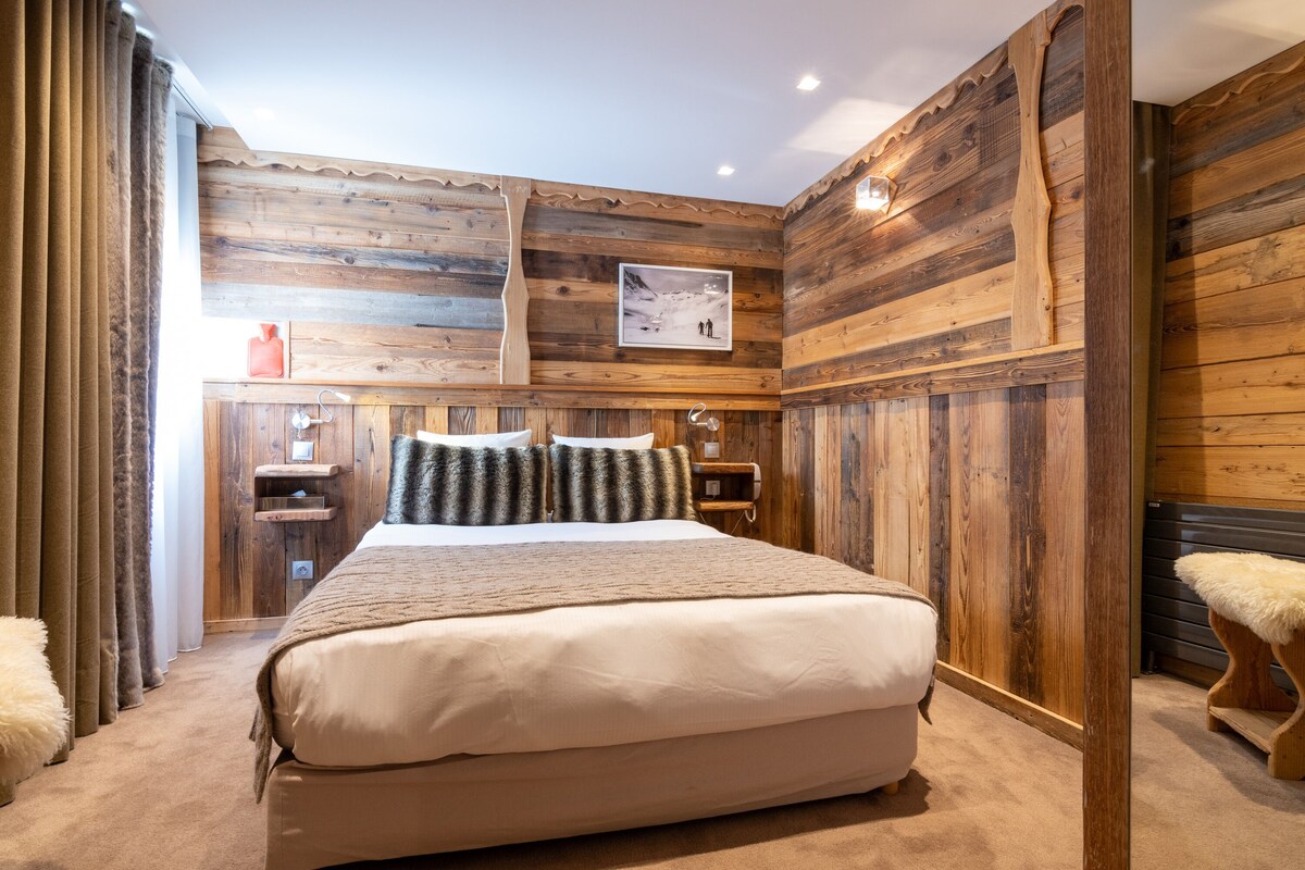 Une chambre aux murs lambrissés, avec un grand lit, une table de chevet et un tableau encadré accroché au mur.