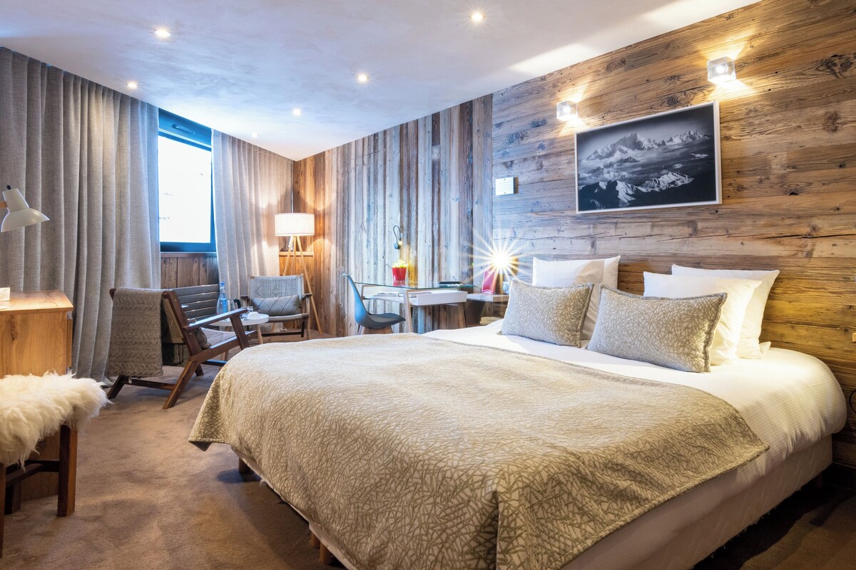 Une chambre d’hôtel avec un grand lit, un bureau, une chaise et un mur en bois orné d’un tableau.