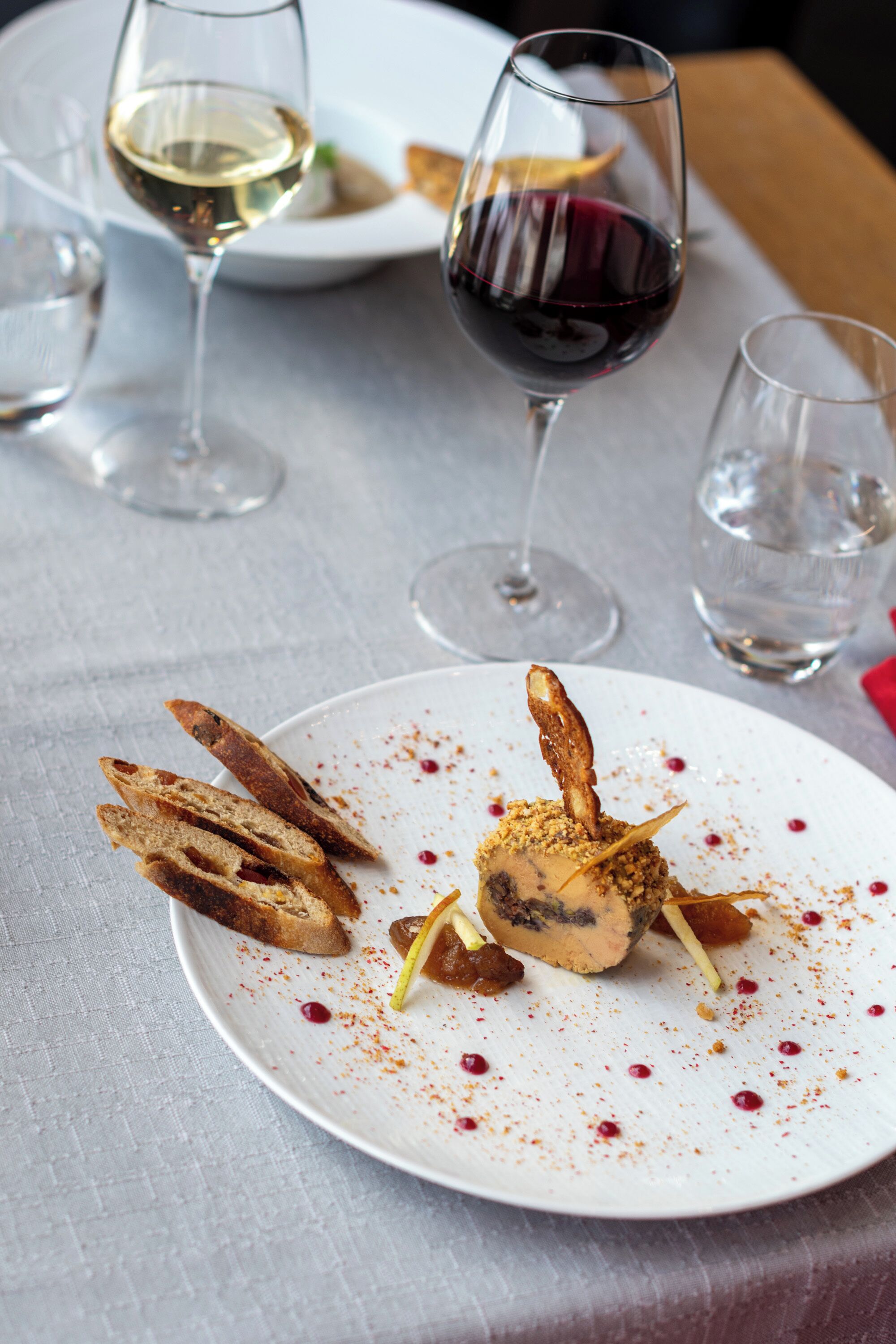 A dining table with a white plate of food, two wine glasses, and a water glass.