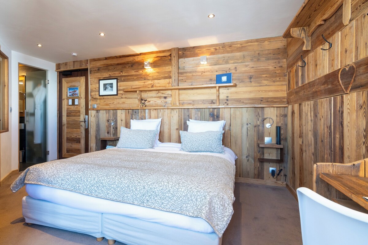 Une chambre avec un grand lit, des murs recouverts de panneaux de bois et une petite table de chevet avec une lampe.
