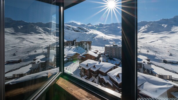 Vista desde una ventana con paisaje montañoso cubierto de nieve, edificios y pistas de esquí.