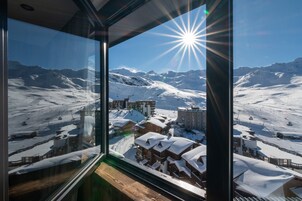 A view from a window overlooking a snow-covered mountain landscape with buildings and ski slopes.