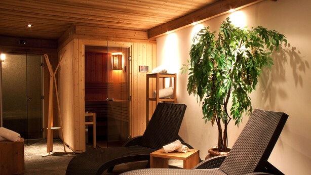 Un área de spa con dos sillones reclinables, un banco de madera, una mesita con una toalla y una planta en maceta.
